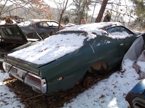 1974 Dodge Challenger - This green car sits in a snowy junkyard with other vehicles.