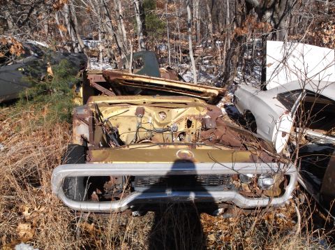 1974 Dodge Challenger - Front view of a heavily rusted 1974 Dodge Challenger in a junkyard setting, with other vehicles visible.