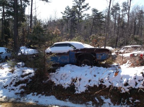 1974 Dodge Challenger - A blue 1974 Dodge Challenger sits in a snowy junkyard, partially obscured by trees and snow.