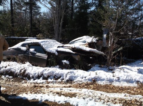 1974 Dodge Challenger - Two abandoned cars sit in a snowy wooded area, showing significant damage.