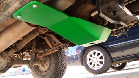 1993 Ford Bronco - A green skid plate is mounted under the frame of a vehicle, with another car parked nearby.