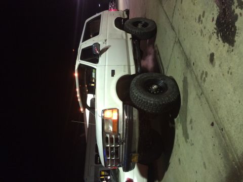 1994 Ford Bronco - A white van with oversized tires is parked on a concrete surface at night.