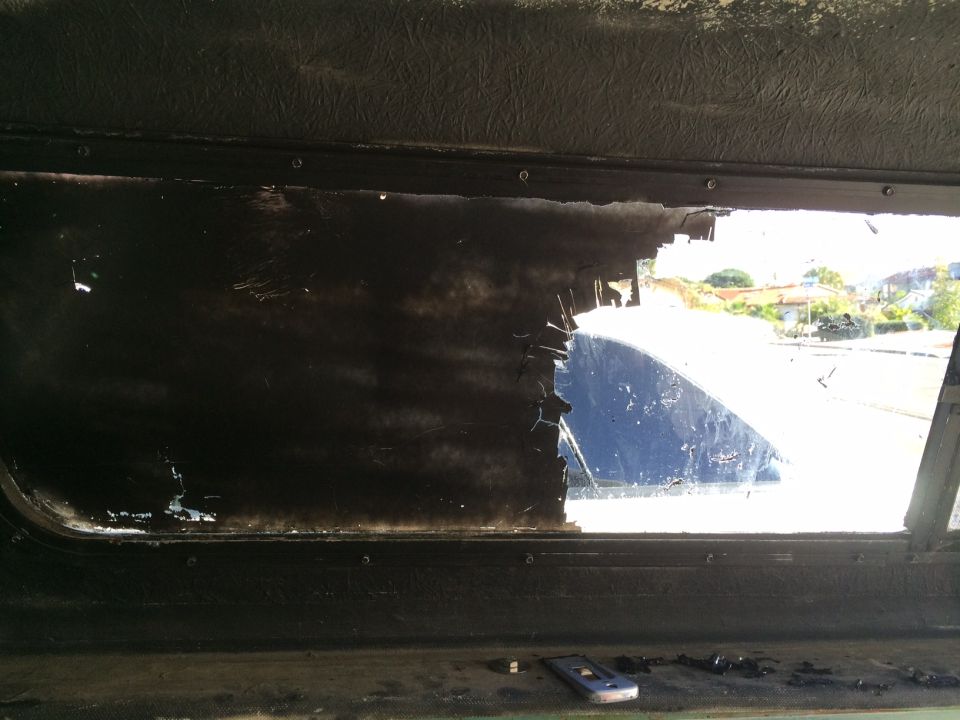 Interior view of a dark vehicle cabin looking through a broken window at a blue vehicle exterior