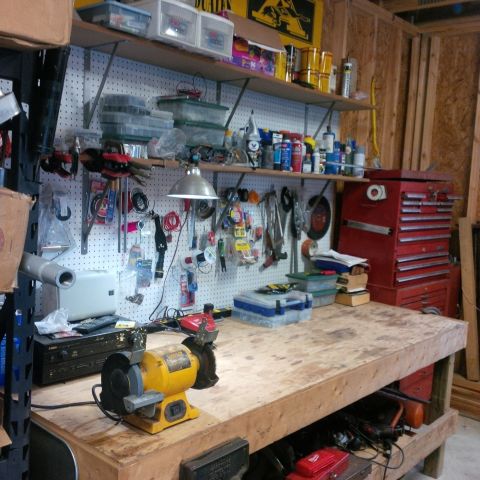 1978 Ford Bronco - A cluttered workbench in a garage, filled with tools, storage bins, and a red toolbox.