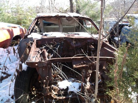 1974 Dodge Challenger - This heavily rusted vehicle sits abandoned in a snowy junkyard, its front end completely exposed.