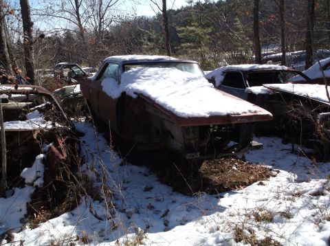 1974 Dodge Challenger - Multiple old cars sit abandoned in a snowy junkyard.