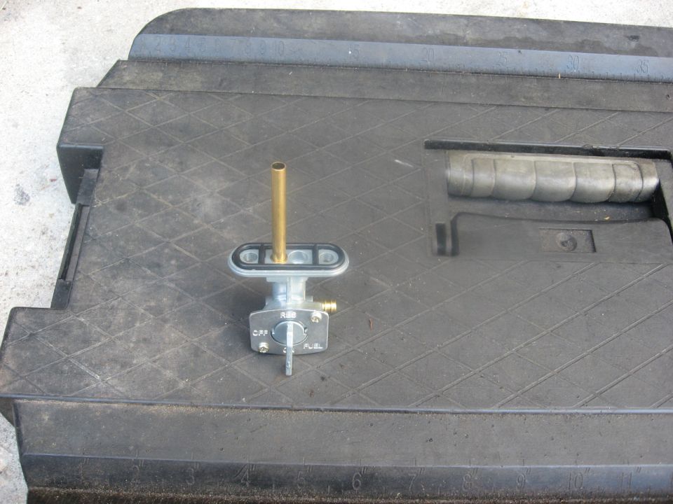 Fuel petcock valve with brass tube and lever set to OFF, on a textured black surface