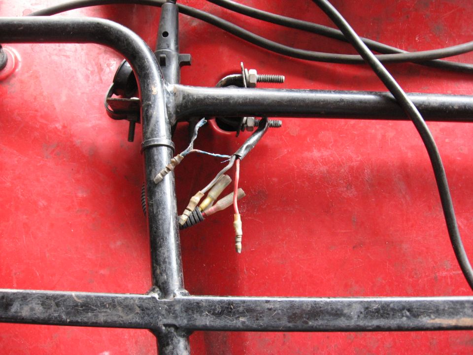 Disconnected bullet-connector wiring at black ATV rack bracket over red plastic fender