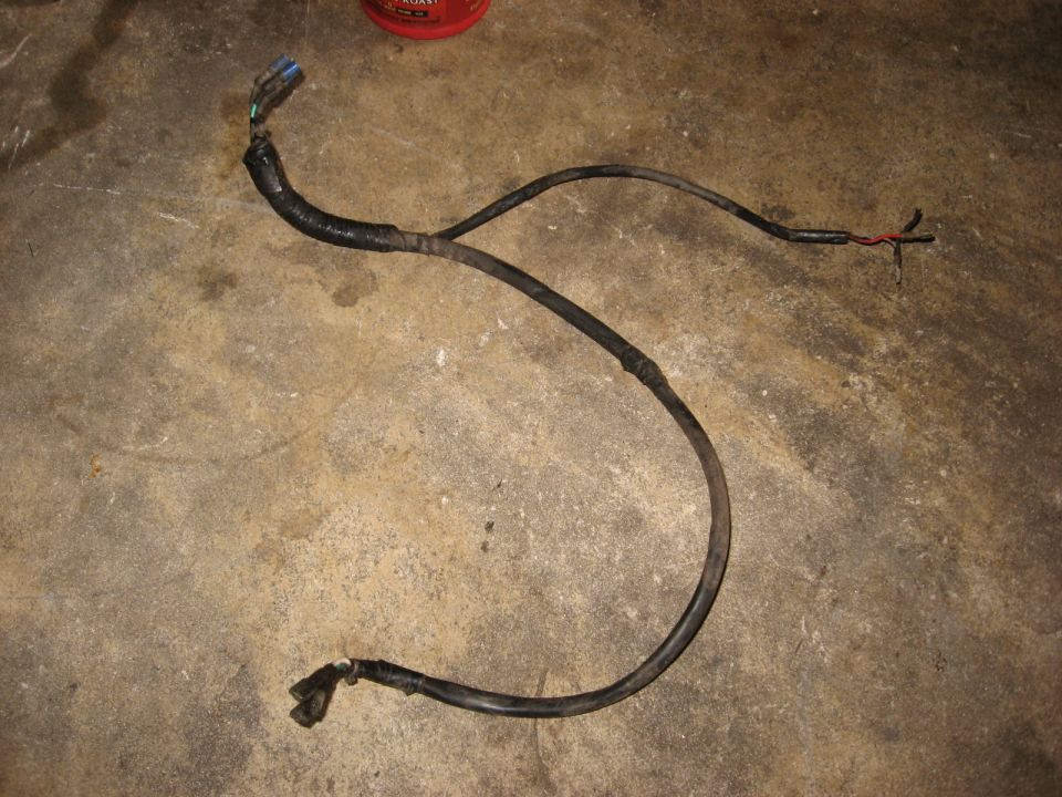 Black wiring harness with blue/green connectors and exposed red/black wires on concrete