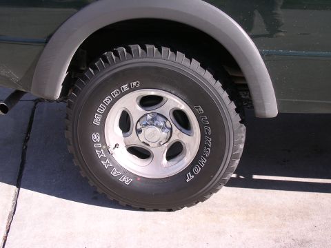 1985 Ford Bronco - Close-up of a tire and wheel on a dark green SUV.