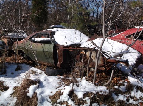 1974 Dodge Challenger - An abandoned green coupe sits partially covered in snow and surrounded by trees. The vehicle is heavily rusted and appears to be missing it…
