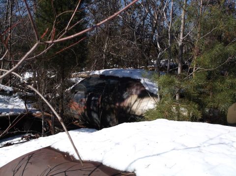 1974 Dodge Challenger - A rusted out 1974 Dodge Challenger is partially covered in snow and surrounded by trees. The vehicle appears to be in a wooded area, with b…