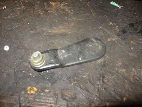 1994 Ford Bronco - A black metal linkage part with a ball joint is shown resting on a dirty, wooden surface. A small silver screw is visible to the left of th…