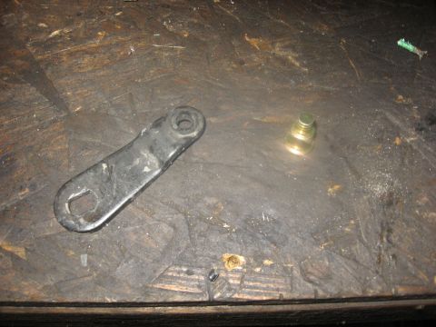 1994 Ford Bronco - A black metal bracket with two holes and a small brass fitting with stacked rings sit on a dark, textured wooden surface.
