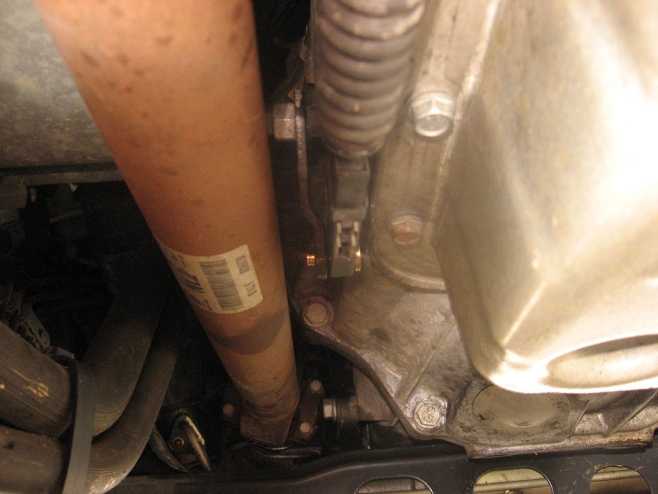 Underside view of a vehicle driveshaft and transmission housing with a label on the driveshaft.