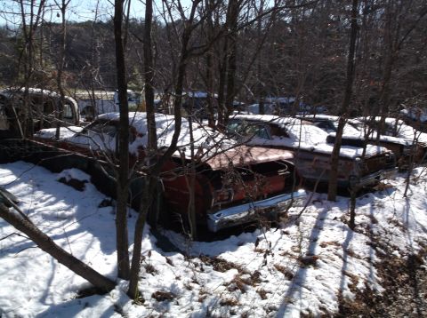 1974 Dodge Challenger - Several vintage cars are parked in a snowy wooded area. The closest car is a red coupe with its hood open, showing some chrome trim on the…