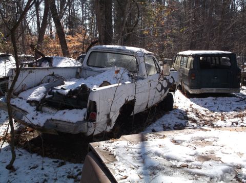1974 Dodge Challenger - Two abandoned vehicles, a white pickup truck and a dark van, sit in a snowy wooded area. The pickup truck has flame decals on its side and…