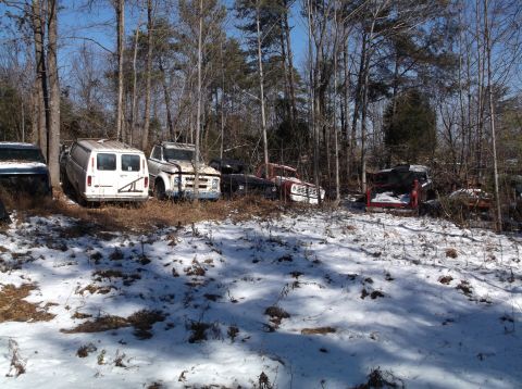 1974 Dodge Challenger - A collection of abandoned vehicles, including a white van and several pickup trucks, sit in a snowy wooded area under a clear blue sky.