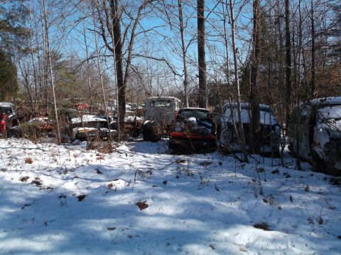 1974 Dodge Challenger - A collection of abandoned vehicles, mostly trucks and vans, are parked in a snowy wooded area. The vehicles are in various states of disrep…