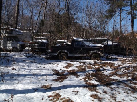 1974 Dodge Challenger - Several old pickup trucks and a camper van are parked in a wooded area covered in snow. The trucks appear to be abandoned and are in variou…
