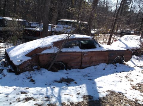 1974 Dodge Challenger - A rusty, snow-covered vintage car sits abandoned in a wooded area. The car appears to be a two-door coupe with visible damage and missing p…