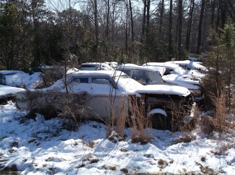 1974 Dodge Challenger - Multiple old vehicles sit abandoned and covered in snow amongst trees.