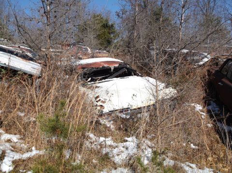 1974 Dodge Challenger - A white classic car, likely a coupe, is partially buried in dry grass and snow. The vehicle's windshield is broken, and the roof appears to…