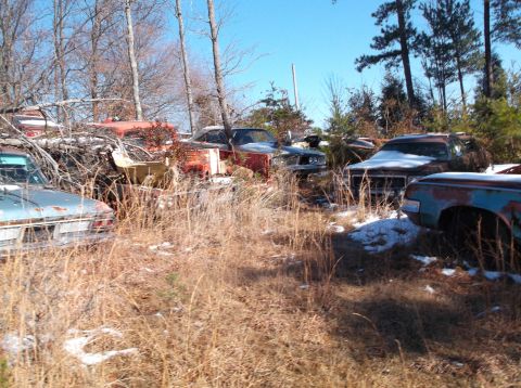 1974 Dodge Challenger - A collection of abandoned vehicles sits in a dry, grassy field with scattered patches of snow. The vehicles are various makes and models, i…
