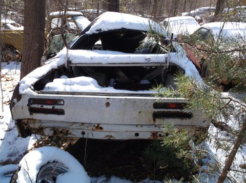 1974 Dodge Challenger - The rear of a white, rusty 1974 Dodge Challenger is covered in snow, with its trunk open and interior visible. The car is parked outdoors i…