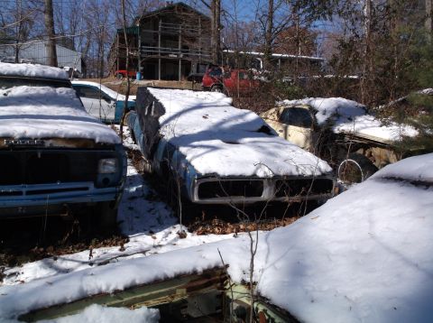 1974 Dodge Challenger - Several snow-covered vehicles are parked in a wooded area, with a large house visible in the background. The closest vehicle is a light blu…
