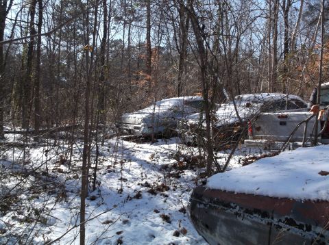 1974 Dodge Challenger - Two old vehicles, partially covered in snow, sit abandoned in a wooded area. The vehicle in the foreground is a pickup truck, and another v…