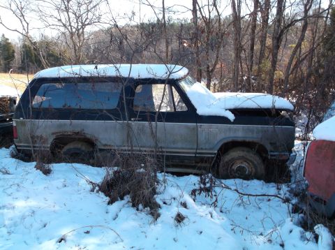 1974 Dodge Challenger - A weathered, two-tone SUV, possibly a Dodge Ramcharger, sits partially buried in snow and brush. The vehicle has a black top half and a fad…