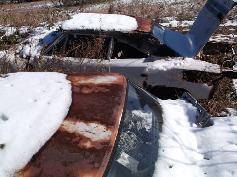 1974 Dodge Challenger - Two rusty, snow-covered vehicles are parked outdoors in a dry, grassy field. The vehicle in the foreground is a coupe with a prominent rust…