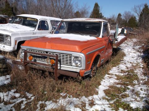 1974 Dodge Challenger - An orange pickup truck with a snow-covered hood and windshield is parked next to a white pickup truck in a snowy, wooded area.