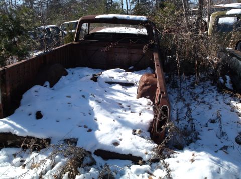 1974 Dodge Challenger - A rusty, abandoned pickup truck bed is partially covered in snow and surrounded by dry brush. Other vehicles are visible in the background…