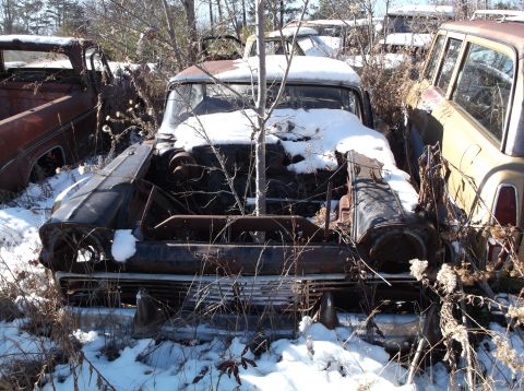 1974 Dodge Challenger - A weathered and rusted car sits in the snow with its hood open, revealing the engine. The vehicle is surrounded by bare branches and dry br…