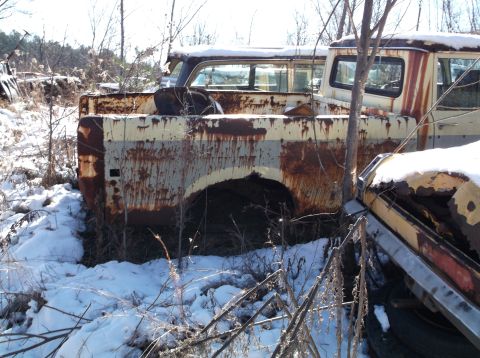 1974 Dodge Challenger - The rear section of a heavily rusted, two-tone yellow and white pickup truck is visible in a snowy, wooded area. The truck bed shows signif…