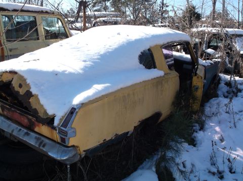 1974 Dodge Challenger - A yellow coupe covered in snow sits in a junkyard with other vehicles visible in the background. The rear tail light and chrome bumper are…