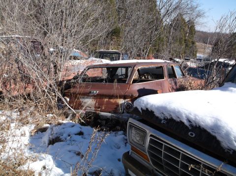 1974 Dodge Challenger - Several heavily rusted abandoned vehicles are visible in a snowy wooded area. A brown station wagon with its windows missing is in the fore…