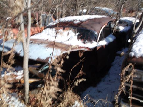 1974 Dodge Challenger - A rusty, snow-covered vintage car sits abandoned amongst trees and dry brush. The vehicle appears to be a coupe with significant body damag…
