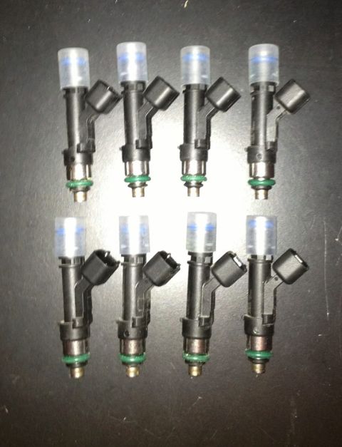1998 Ford Crown Victoria - Eight automotive fuel injectors with green O-rings and black connectors arranged in two rows on a dark surface.