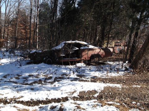 1974 Dodge Challenger - A rusty, abandoned 1974 Dodge Challenger sits in a wooded area covered in snow. The car is heavily weathered, with missing parts and overgr…