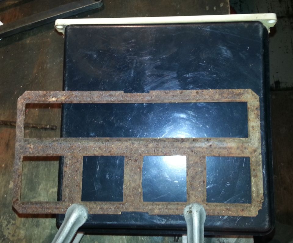 Rusty metal bracket with four square openings on a black container.