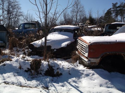 1974 Dodge Challenger - Several old vehicles are parked in a snowy junkyard under a clear blue sky. A blue pickup truck is visible in the background, with a dark-c…