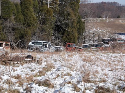 1974 Dodge Challenger - Several old, rusted vehicles are parked in a snowy field with trees in the background. One vehicle in the foreground appears to be a dark-c…
