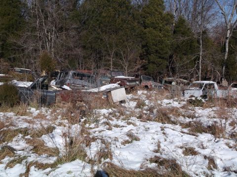 1974 Dodge Challenger - A collection of rusted and weathered vehicles, mostly trucks and SUVs, sit abandoned in a snowy, wooded area. The vehicles appear to be fro…
