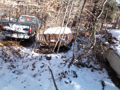 1974 Dodge Challenger - Two old vehicles, a pickup truck and a coupe, sit partially covered in snow and surrounded by bare trees in a wooded area. The rear of the…
