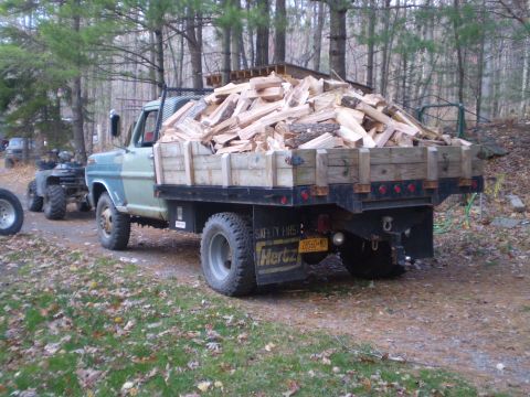 1979 Ford Bronco - A flatbed truck loaded with firewood is parked on a dirt road next to an ATV. The truck has a wooden bed extension and a license plate that…