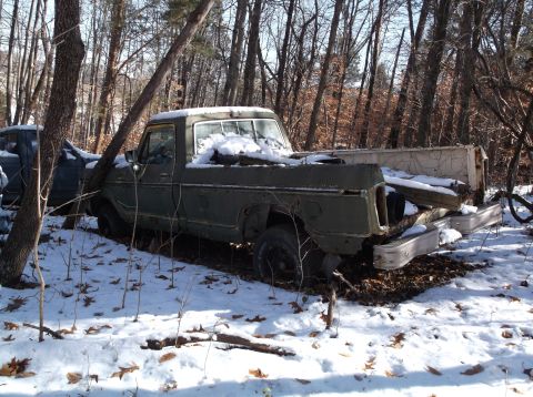 1974 Dodge Challenger - An old, weathered green pickup truck sits abandoned in a snowy wooded area. The truck is partially covered in snow and surrounded by bare t…