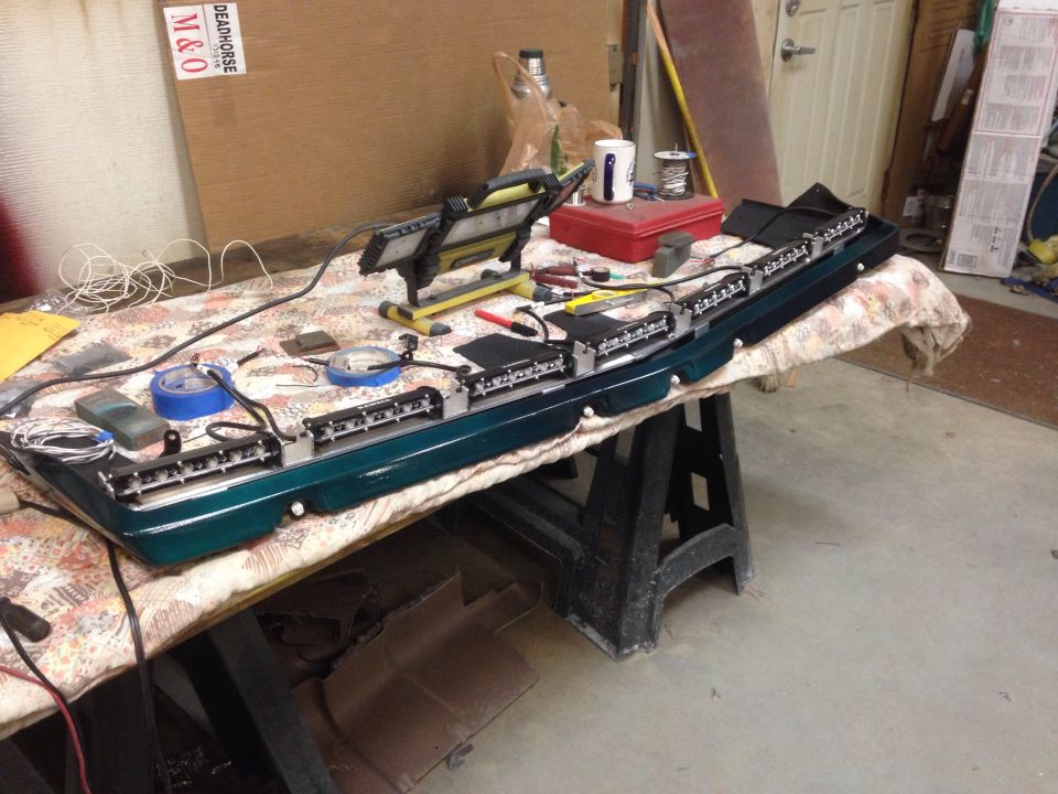 Car part with multiple light bars wired up on a table with tools